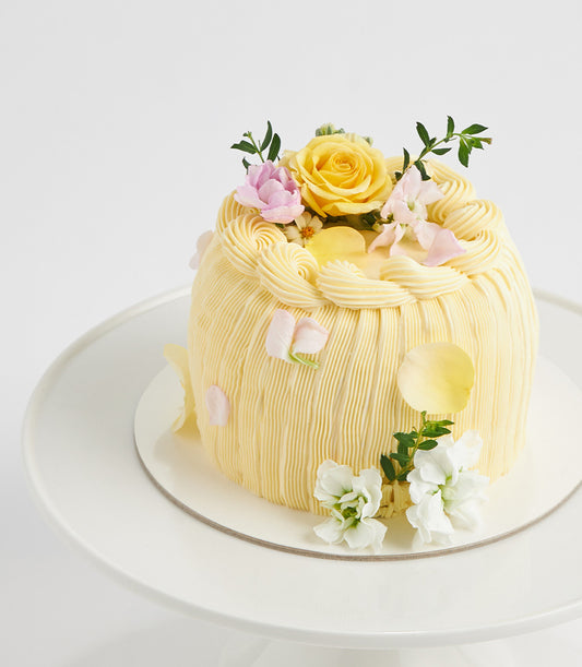 Sunshine yellow layer cake with fresh flowers and piped frosting on white cake stand