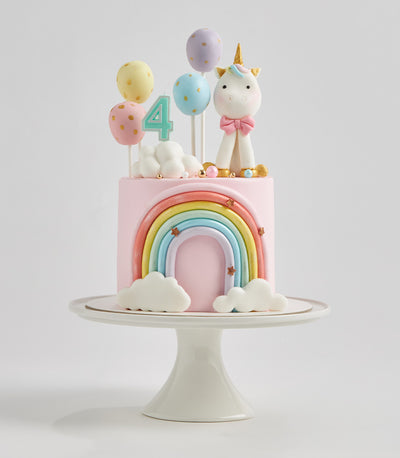 Pastel rainbow unicorn birthday cake with fondant arch, golden stars, and number 4 candle for kids