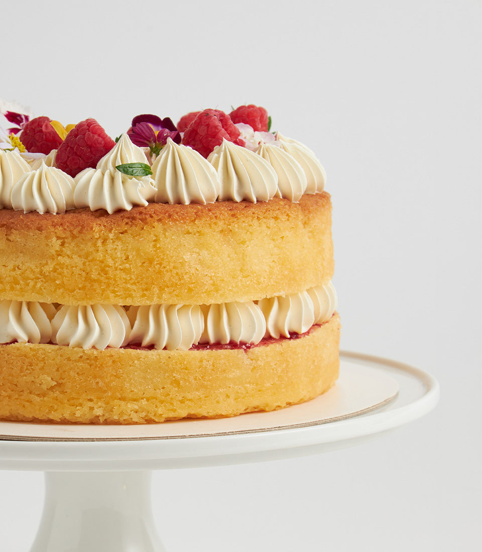 Raspberry buttercream sponge cake with fresh raspberries and edible flowers on white cake stand