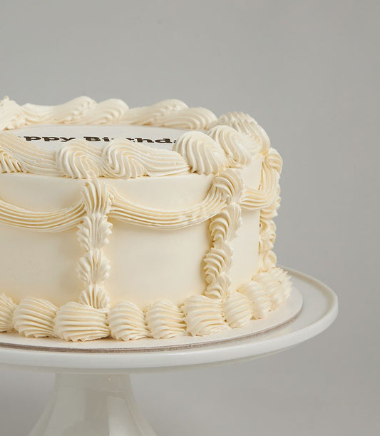 Classic cream border birthday cake with piped frosting swirls and elegant shell designs