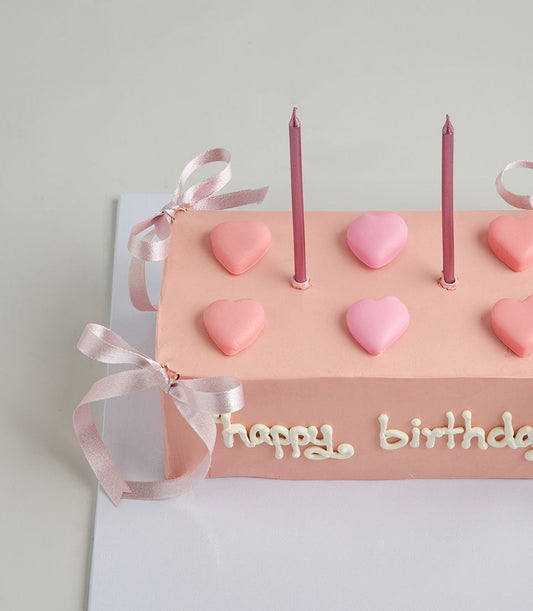 Light pink heart birthday cake with strawberry layers, white icing message, and metallic candles for celebration
