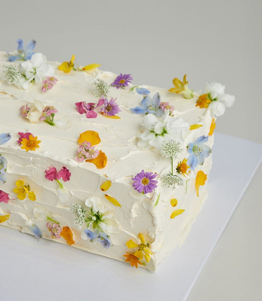 Vanilla cake with white frosting adorned with edible flowers in purple, pink, and yellow petals