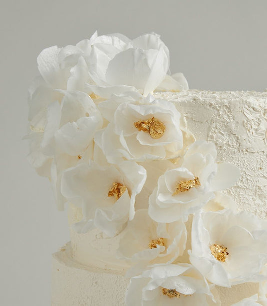 Elegant white two-tier wedding cake with cascading wafer flowers and gold leaf details