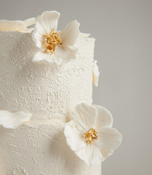 Elegant white fondant wedding cake with delicate sugar flowers and gold leaf accents on tiered design