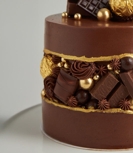 Luxury two-tier dark chocolate ganache cake with Ferrero chocolates, gold leaf, and edible pearls on white board