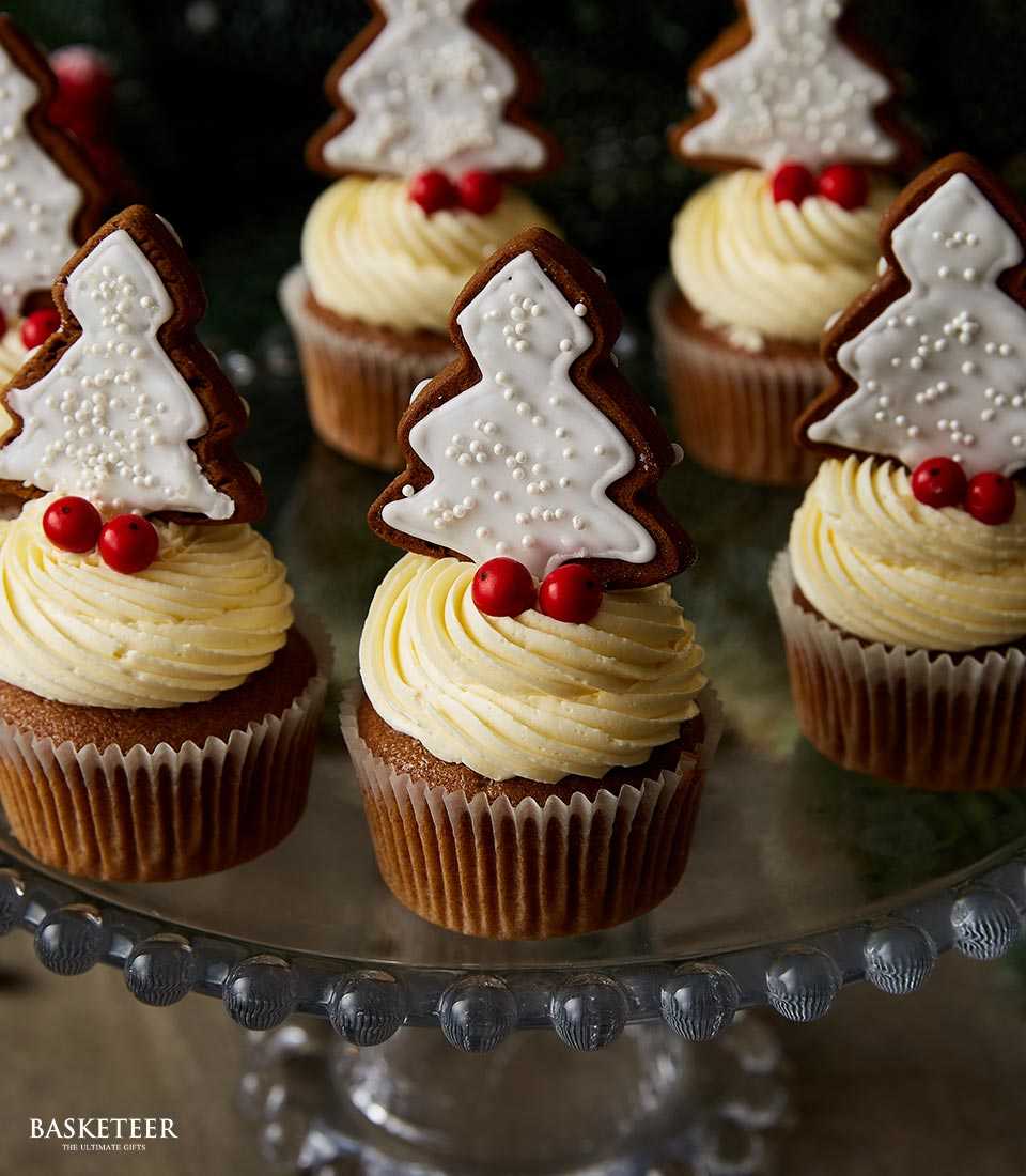 Gingerbread Christmas tree cupcakes with red berries and pale yellow frosting on glass cake stand