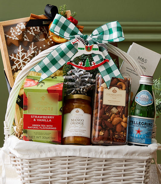 White woven Christmas gift basket with green gingham bow, filled with premium tea, nuts, preserves, and gingerbread cookies