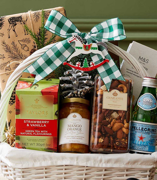 White wicker Christmas wellness basket with gourmet tea, preserves, nuts, and sparkling water tied with green checkered