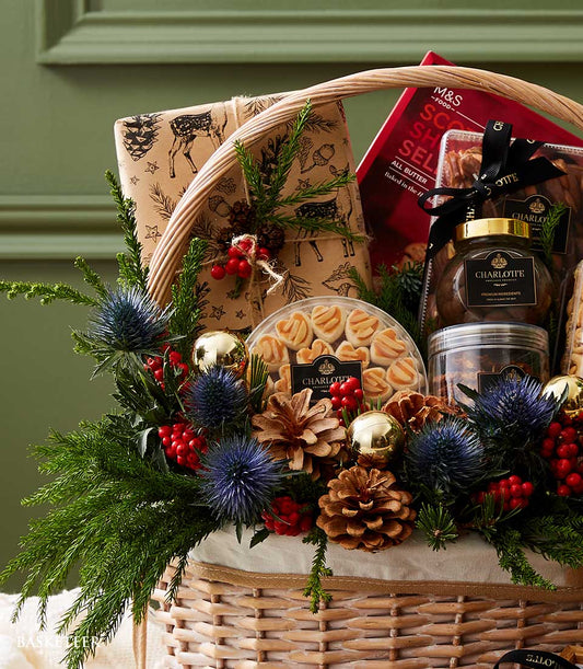 Woven wicker Christmas hamper with gourmet treats, heart-shaped cookies, and festive greenery with gold ornaments