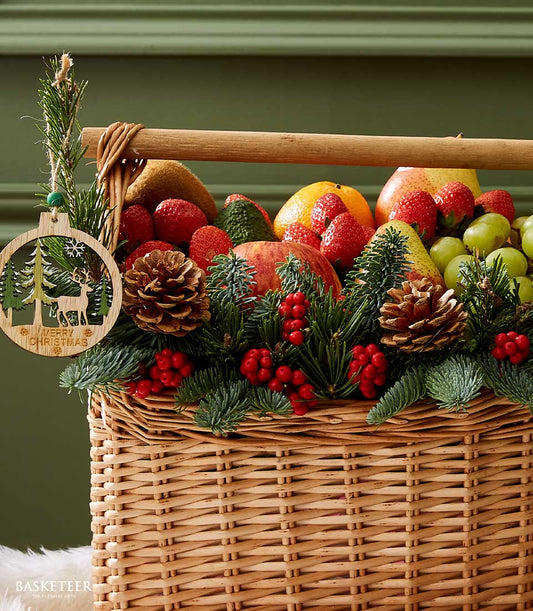 Festive wicker fruit basket with fresh strawberries, grapes, apples, and citrus, decorated with pine branches, red berries,
