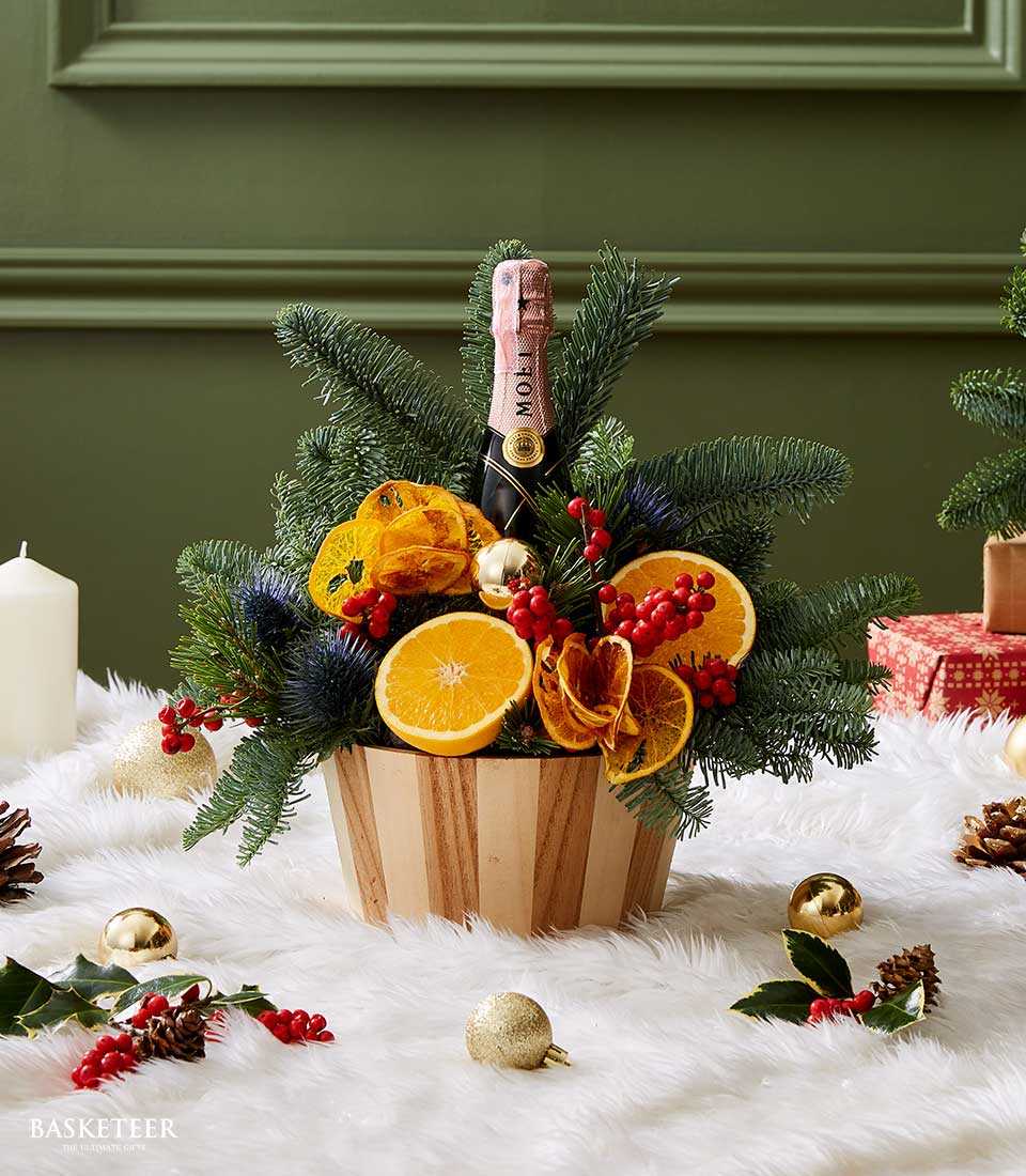 Miniature champagne bottle with fresh pine, red berries, and dried orange slices in luxury wood basket