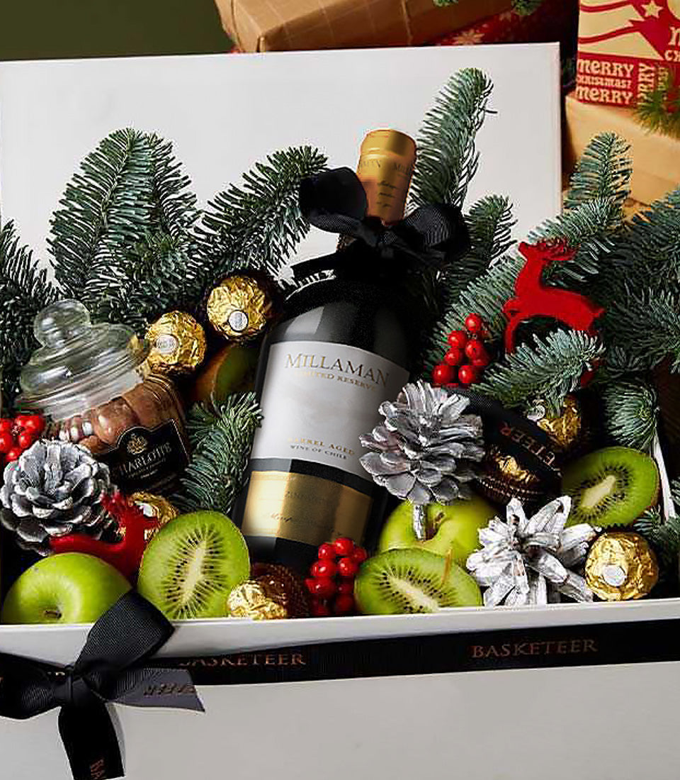 Festive Christmas wine gift box with Millaman red wine, fresh fruits, gold chocolates, and holiday greenery