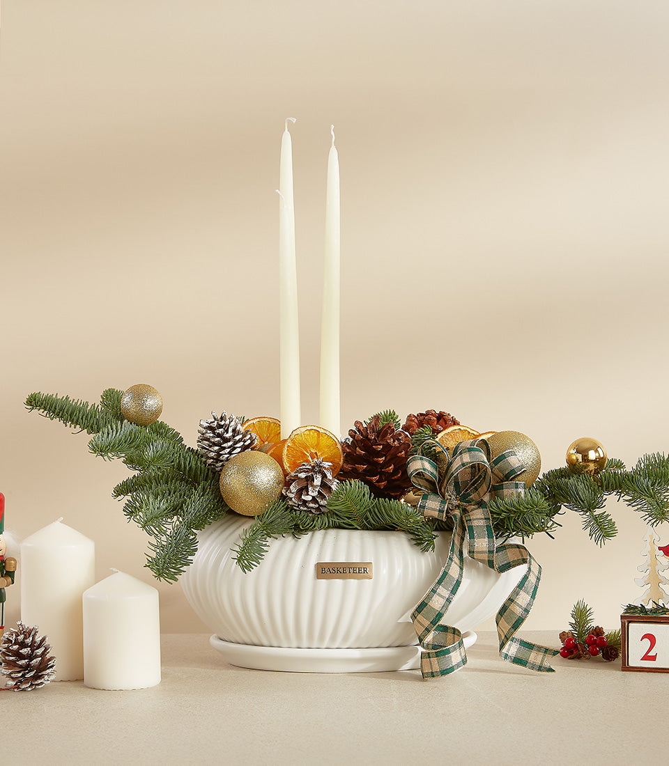 White ceramic holiday centerpiece with fresh fir, gold baubles, pinecones, taper candles and plaid ribbon
