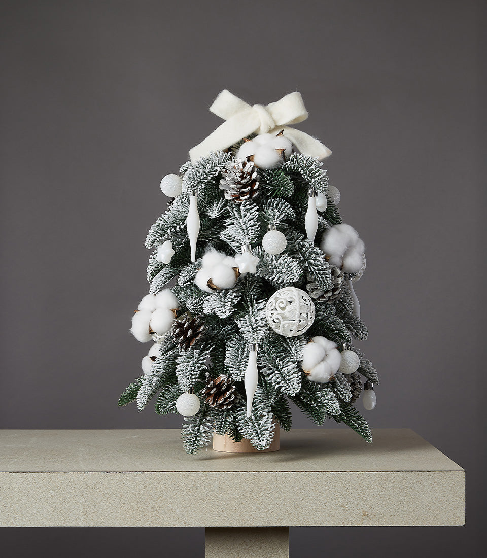 Snowy white flocked Christmas tree with cotton, pinecones, and cream bow ornaments