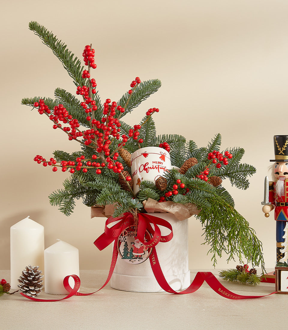 Red berry and pine Christmas arrangement with merry mug, candles, and nutcracker festive display