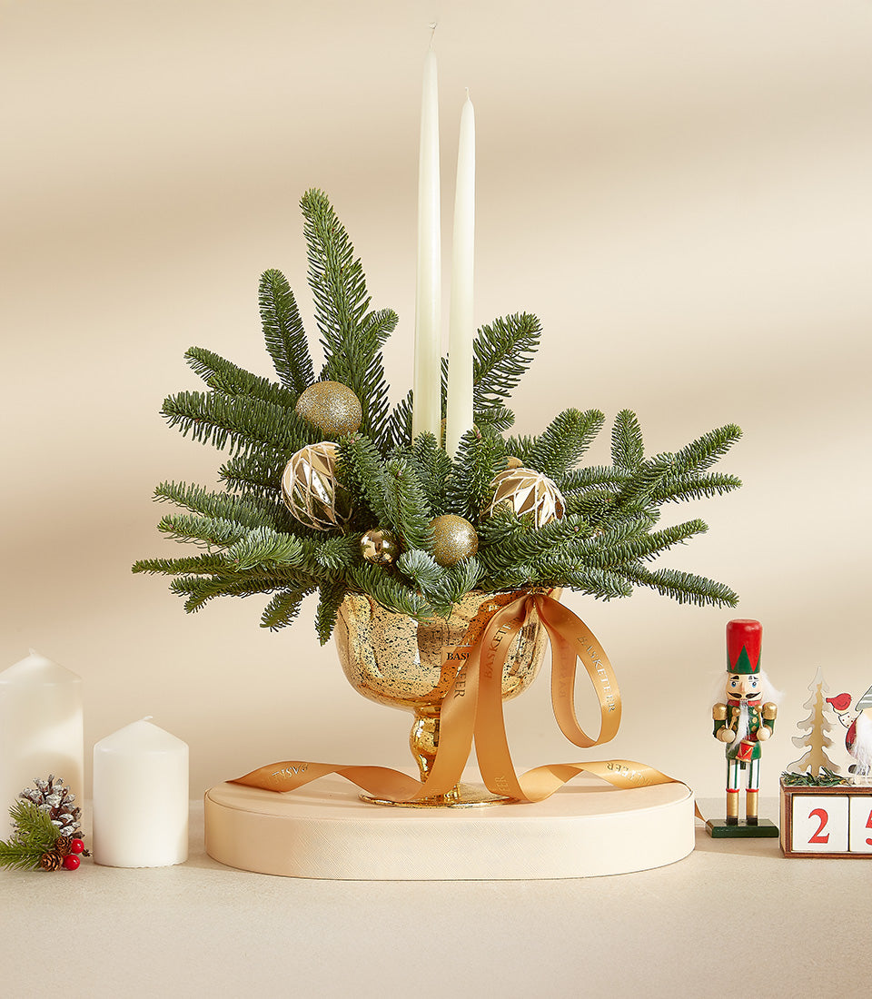 Golden Christmas centerpiece with fir branches, white taper candles, and gold ornaments in textured glass bowl