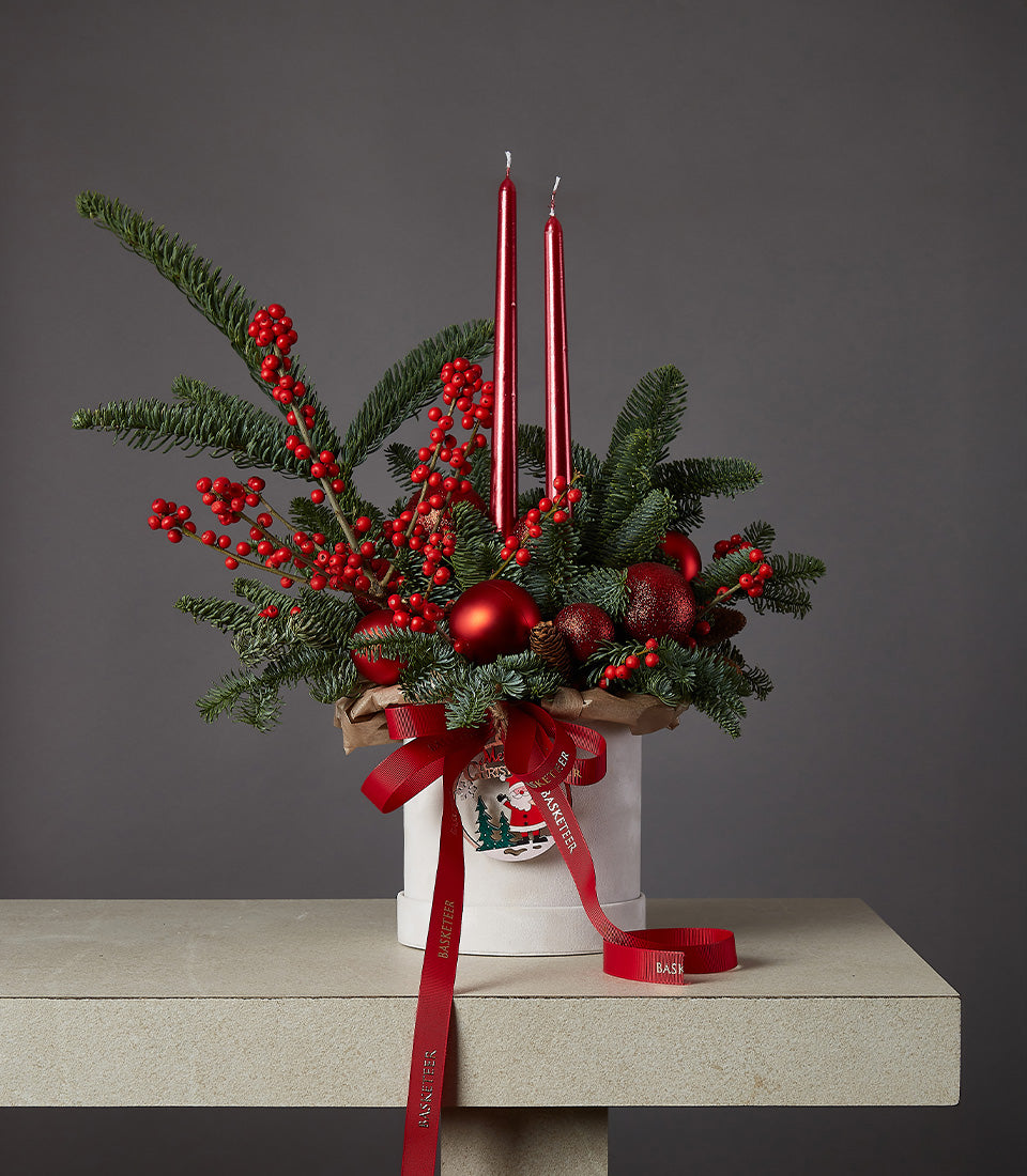Festive red candle Christmas centerpiece with pine branches, berries, and baubles in white box