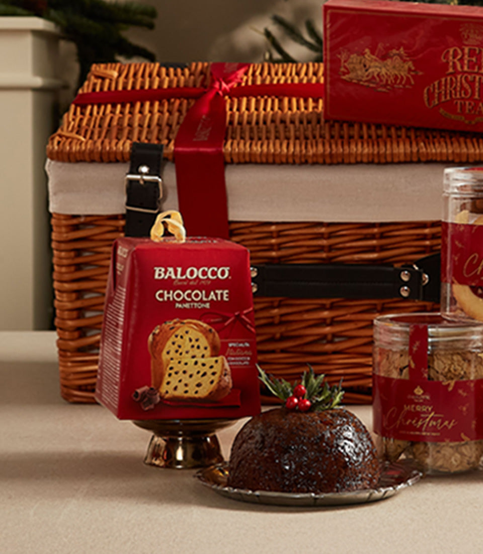 Woven wicker Christmas hamper with leather straps, festive Italian panettone, holly-topped pudding, and gourmet treats