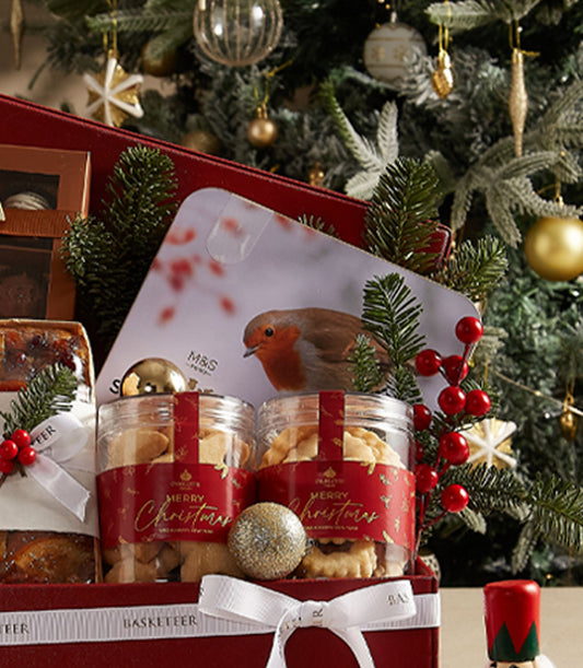 Deep red Christmas hamper with gourmet treats, biscuits in glass jars, fruitcake, chocolates, and festive gold decorations