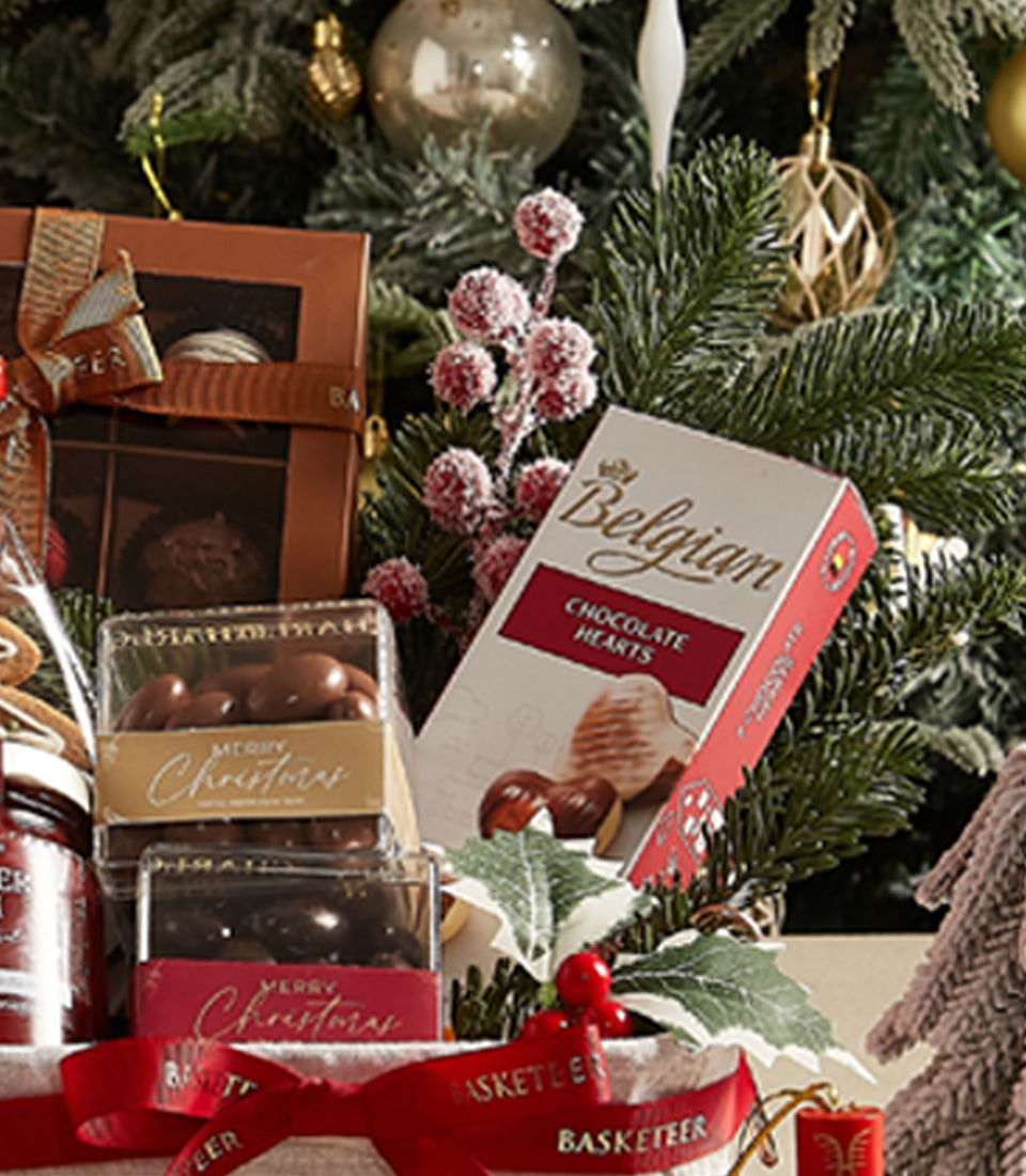 Deluxe Christmas treats basket with Belgian chocolate hearts, gold-trimmed holiday boxes, and festive red ribbon