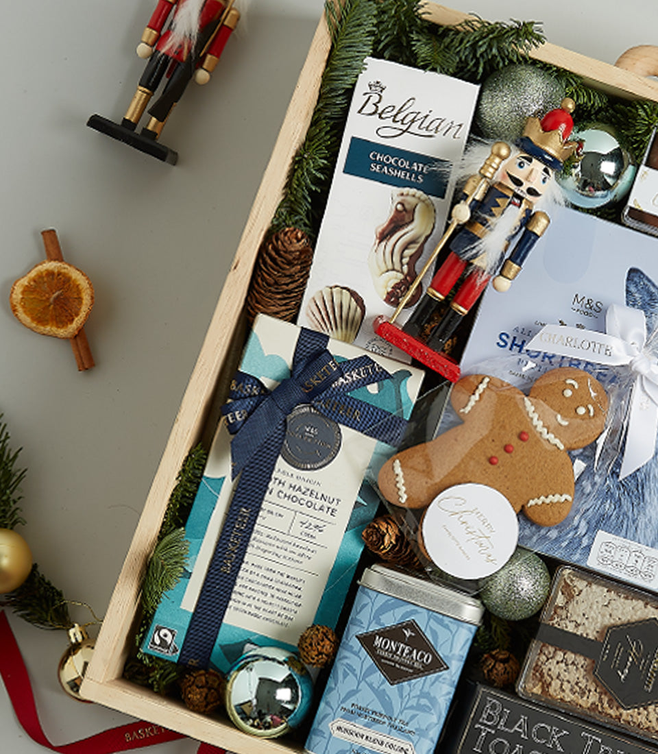 Luxury Christmas hamper in wooden crate with Belgian chocolates, gourmet treats, pine branches, and festive ornaments in