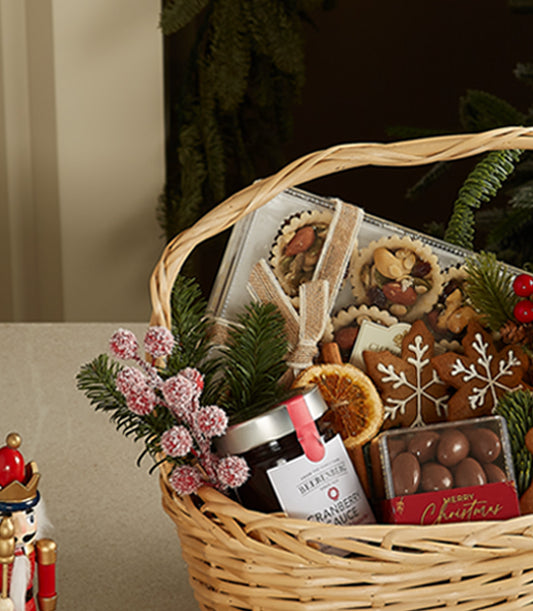 Woven wicker Christmas gift basket with gingerbread cookies, artisan tarts, cranberry sauce, chocolate treats, and festive