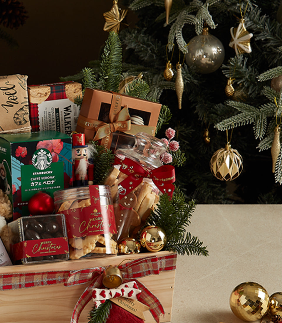 Wooden Christmas gift crate with gourmet coffee, chocolates, cookies, and festive ornaments tied with red plaid ribbon