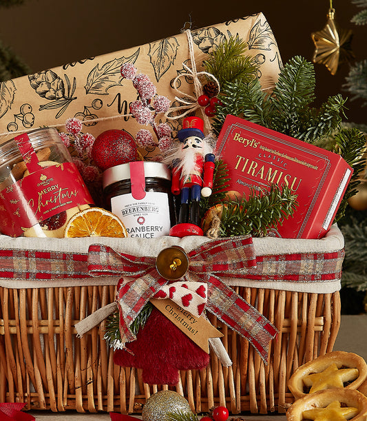 Woven wicker Christmas gift basket with red plaid ribbon, festive treats, and holiday decorations