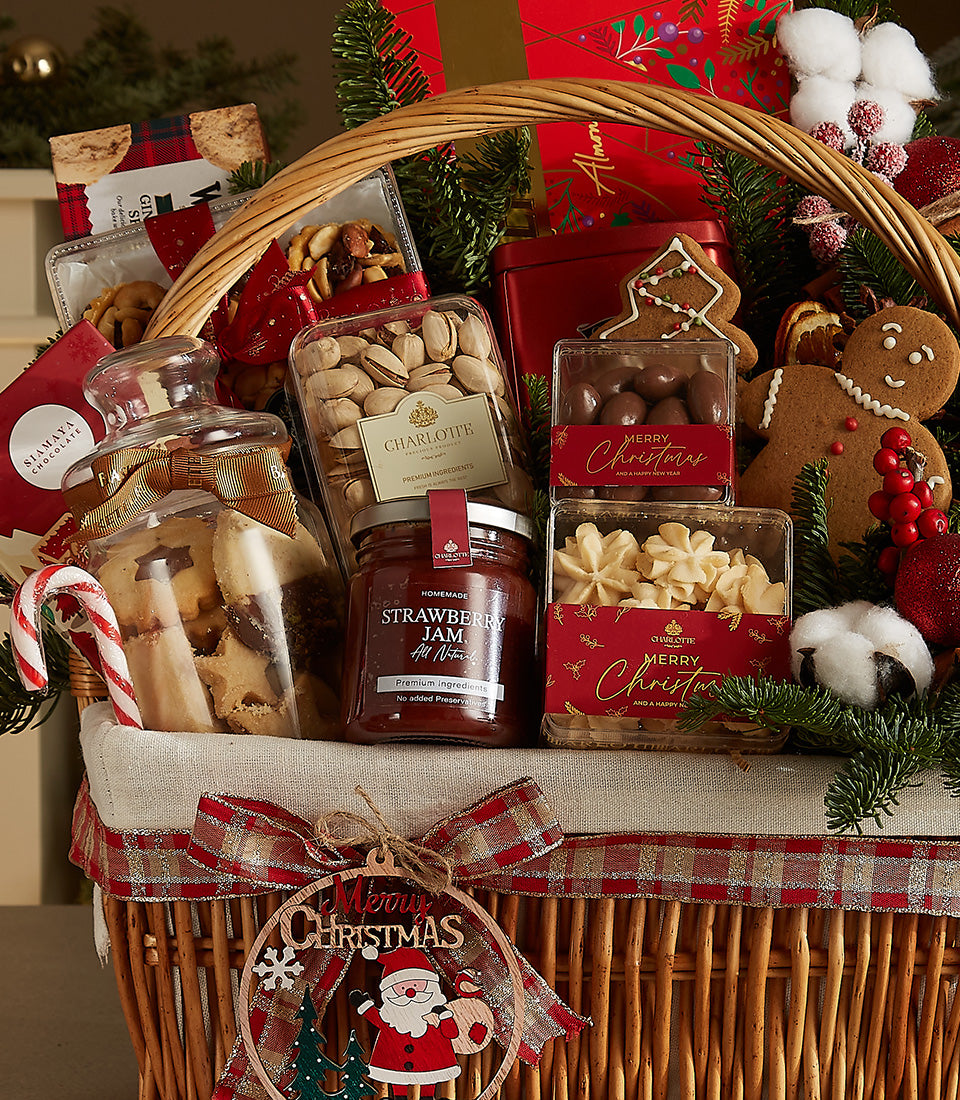 Woven wicker Christmas gift basket with gourmet treats, red and gold plaid ribbon, and festive pine and berry accents