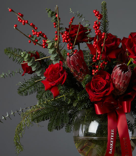 Crimson roses and protea with berry branches in festive Christmas flower arrangement
