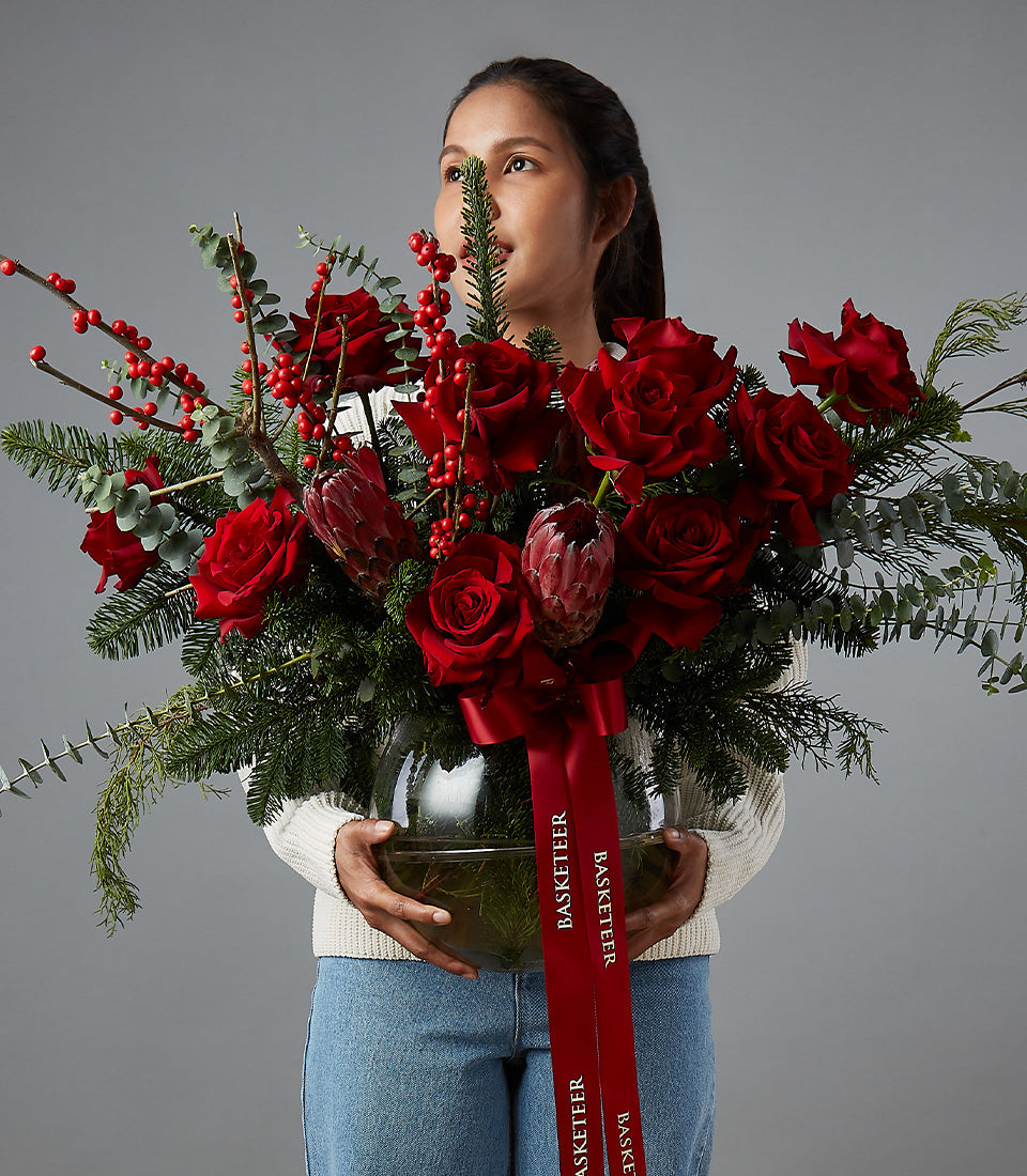 Crimson roses and red protea in festive pine arrangement with red ribbon, premium Christmas flowers