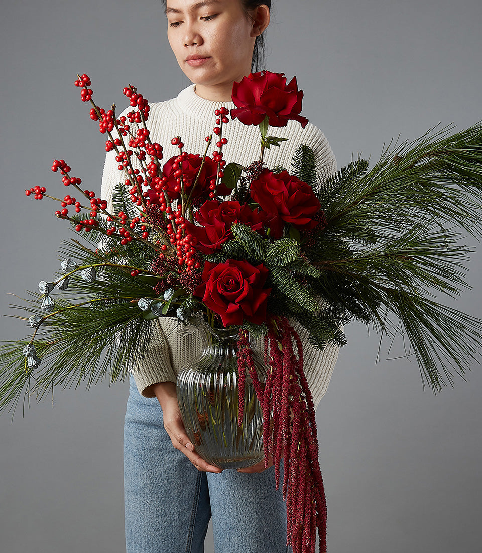 Festive Christmas floral arrangement with deep red roses, berries, and cascading amaranthus in glass vase