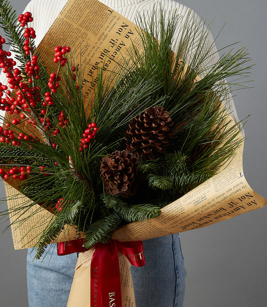 Festive Christmas bouquet with red berries, pine, and pinecones wrapped in brown paper with red ribbon