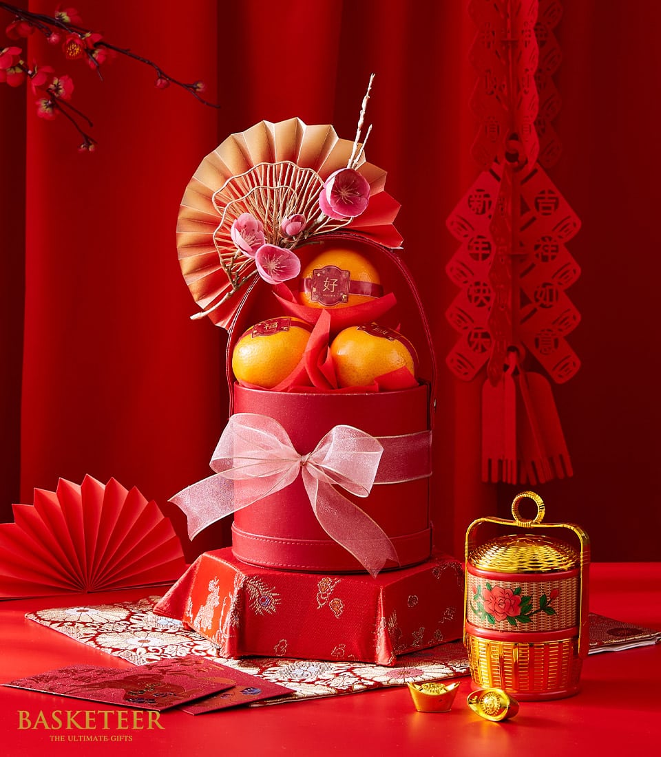 Red mandarin gift box with tangerines, golden fan, and lucky gold ingots for Chinese New Year celebrations
