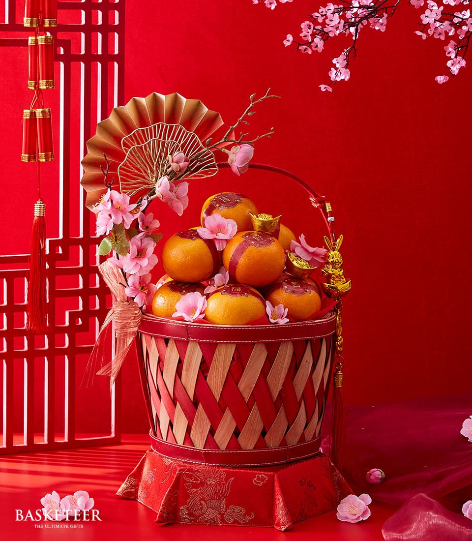 Festive mandarin oranges gift basket with red woven design, gold character tags, and cherry blossoms for Chinese New Year