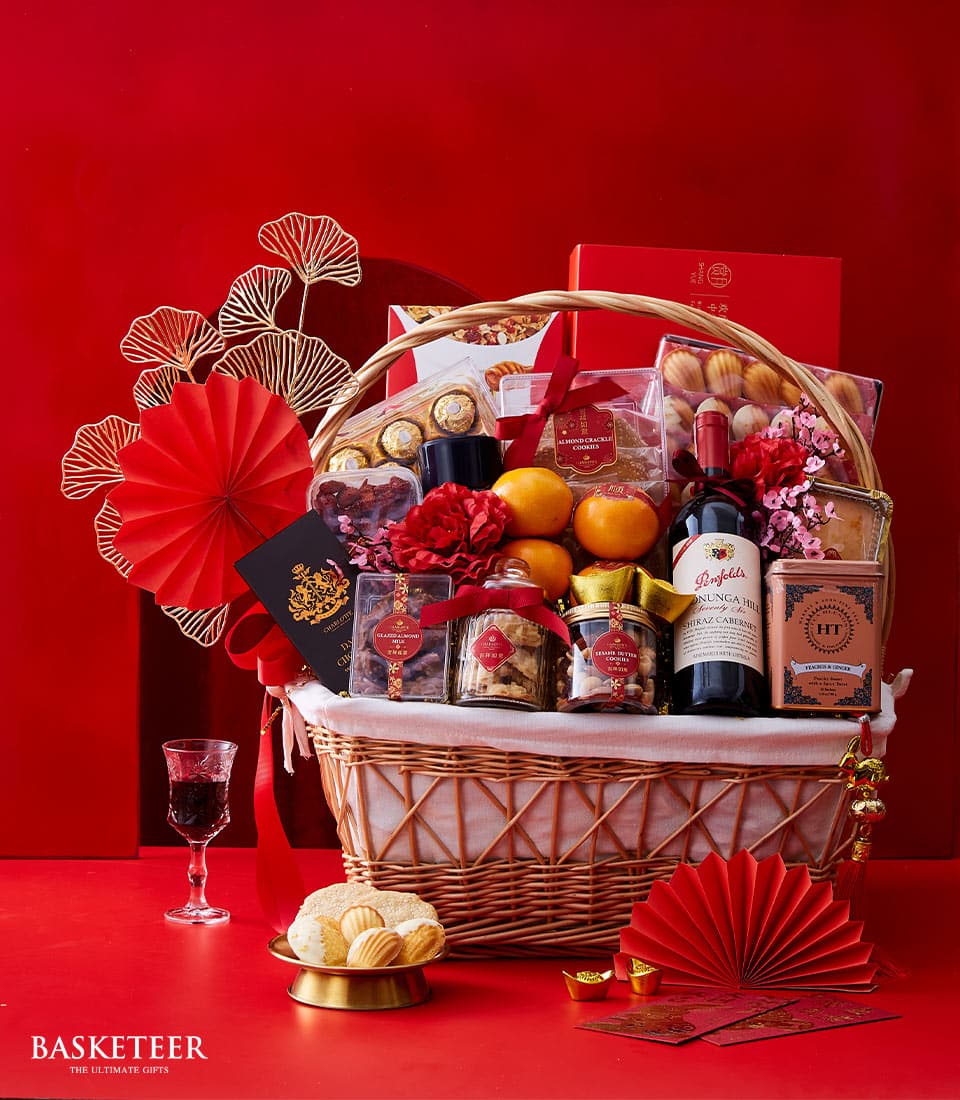 Luxury Chinese New Year wine and treats hamper with red wine, oranges, gourmet cookies, and festive gold ornaments in woven