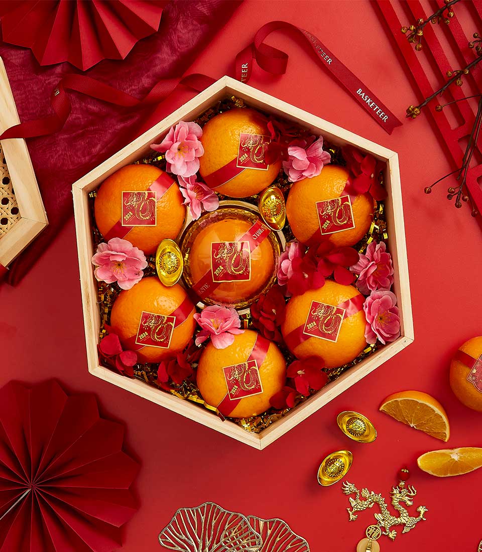 Hexagonal wooden gift box filled with lucky oranges, red ribbons, and gold dragon ornaments for Chinese New Year