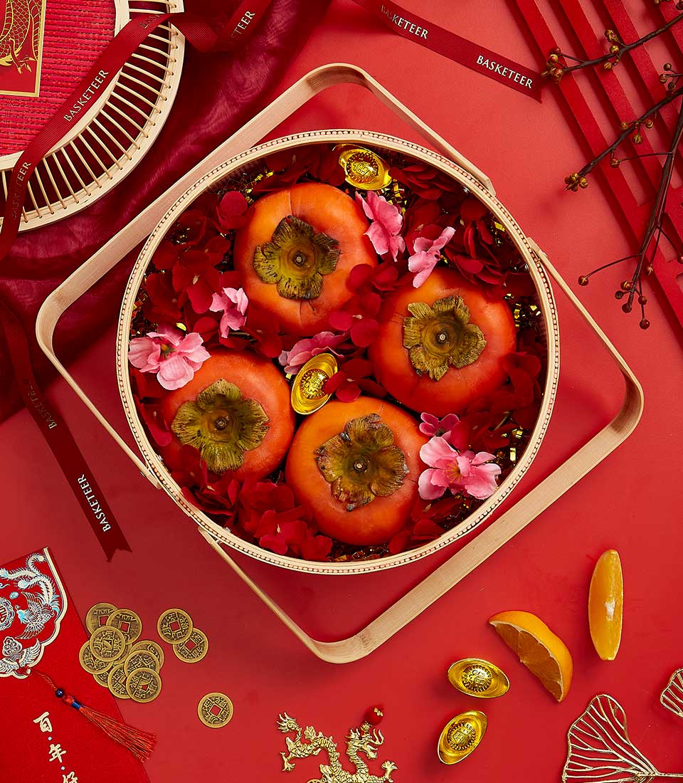 Wooden basket with fresh persimmons, gold ingots, and red petals for Chinese New Year prosperity gifting