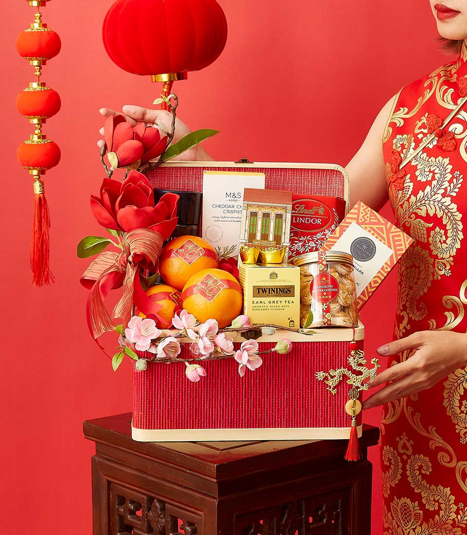 Festive red Lunar New Year gift hamper with gourmet treats, oranges, tea, chocolates, and gold accents