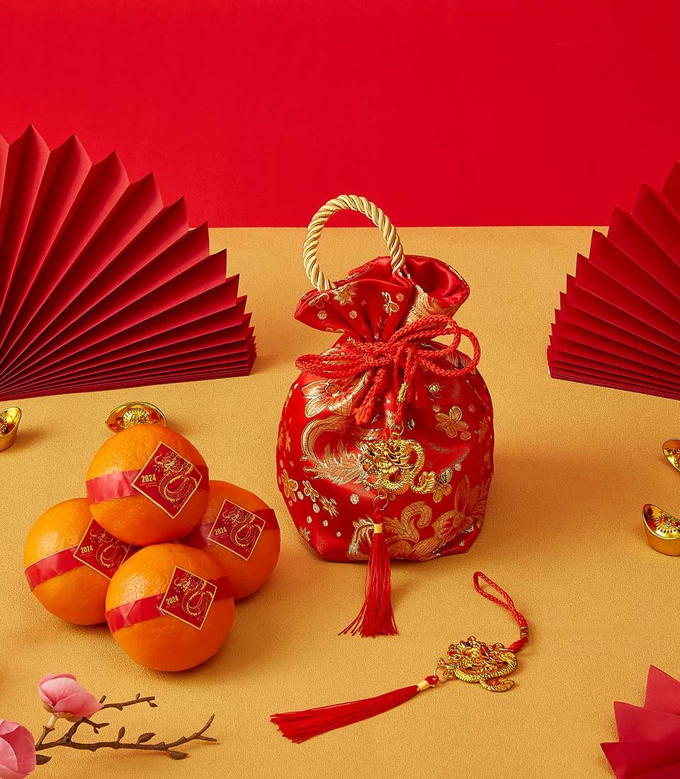 Red satin drawstring pouch with gold dragon embroidery, fresh mandarin oranges, and gold accents for Chinese New Year gifting