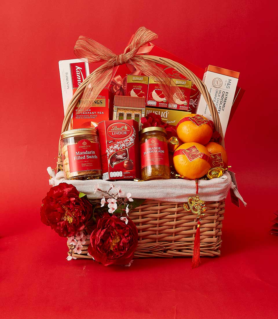 Woven wicker gift basket with red ribbon bow, tea, chocolates, marmalade, fresh mandarins, and gold dragon charm for Chinese