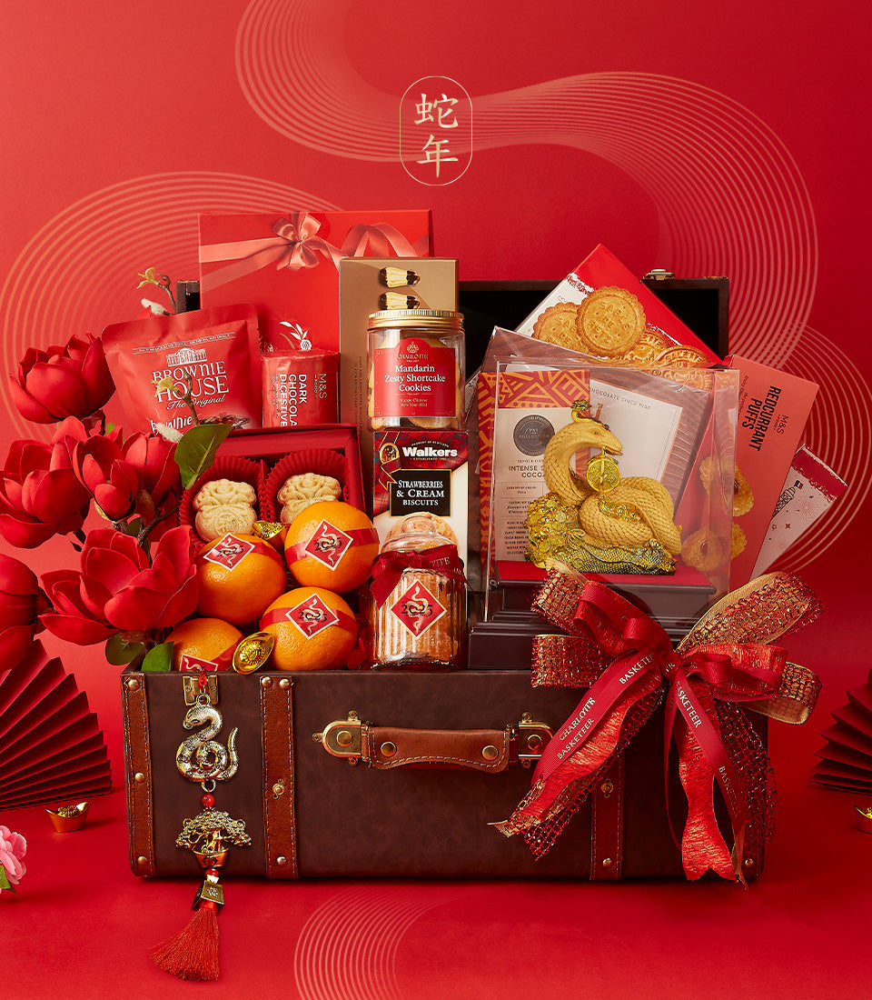 Luxe CNY hamper in vintage brown suitcase with gourmet treats, fresh flowers, mandarin oranges, and golden snake figurine