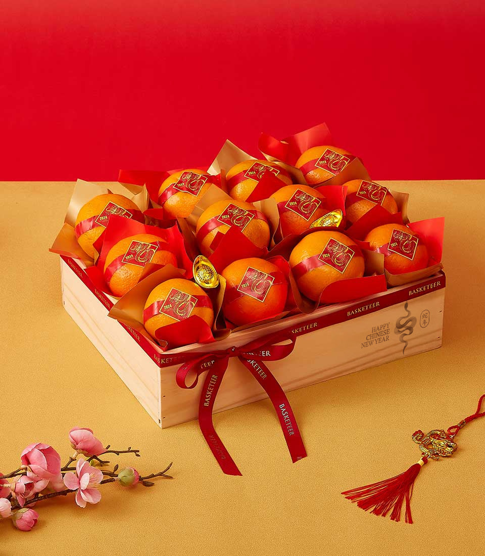 Wooden gift box with twelve wrapped mandarin oranges, gold prosperity ingots, and red ribbons for Chinese New Year