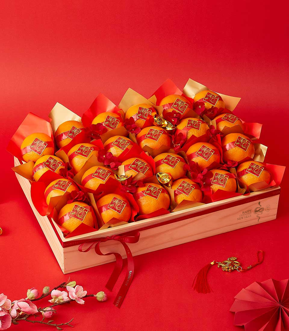 Wooden crate of individually wrapped mandarin oranges with gold ingot charms, red and gold paper, and Chinese New Year