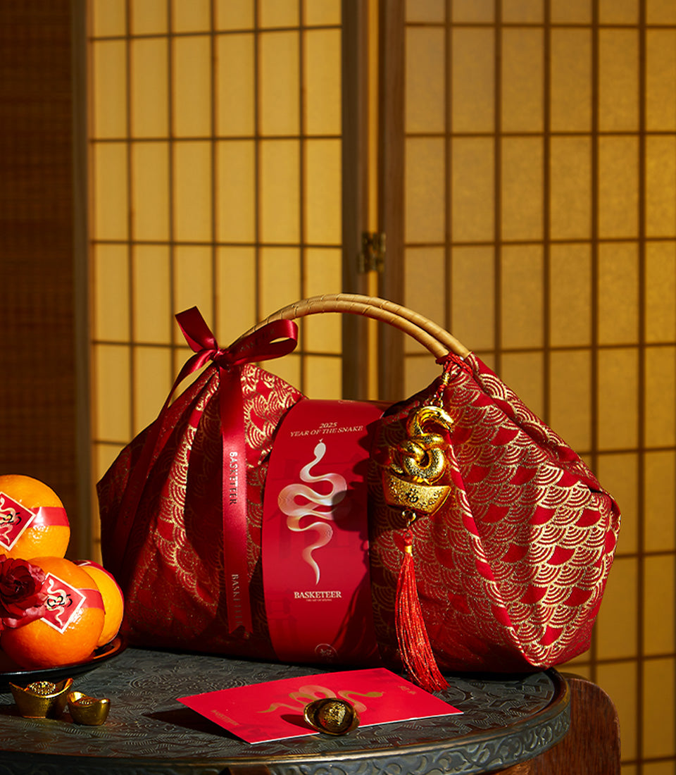 Red and gold Chinese New Year gift bag with bamboo handles, festive oranges, red envelope, and lucky charms for Year of the