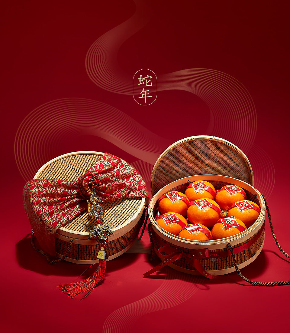 Woven bamboo gift boxes with red and gold fabric bow, silver dragon charm, and bright orange tangerines for Chinese New Year