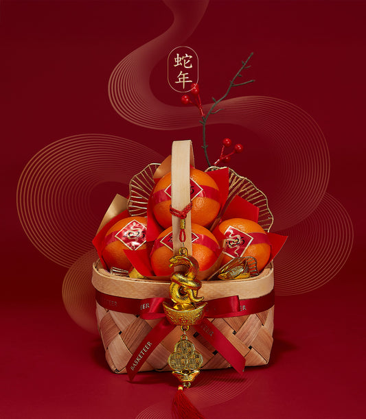 Woven basket with bright orange tangerines tied in red ribbons, gold crinkled paper, and snake-year charm for Chinese New