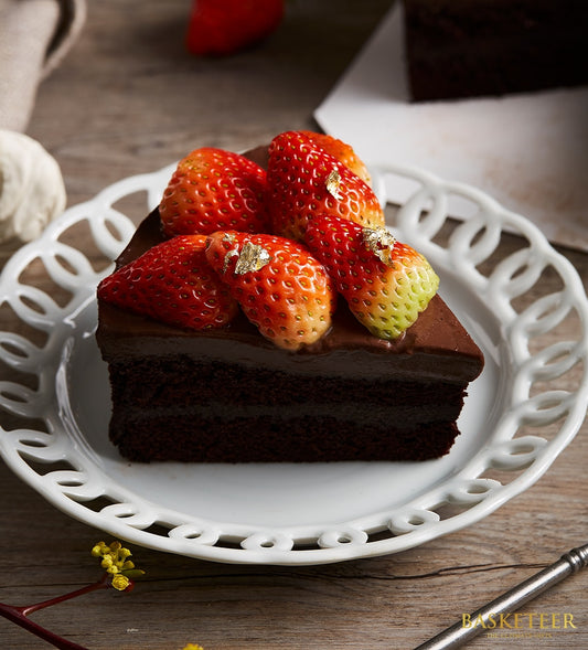 Rich chocolate cake with fresh strawberries and gold leaf on white decorative plate
