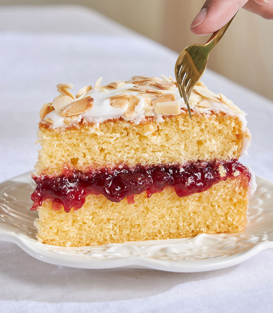 Cherry Bakewell almond cake slice with jam filling and toasted almond topping on scalloped plate