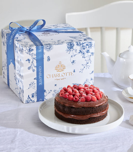 Chocolate raspberry ganache celebration cake with fresh raspberries, presented in luxury gift box with blue floral pattern
